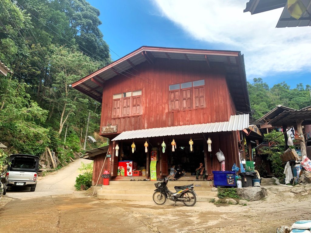 Immagine di una tipica casa in legno tailandese con moto parcheggiata di fronte, immersa nel verde della natura.