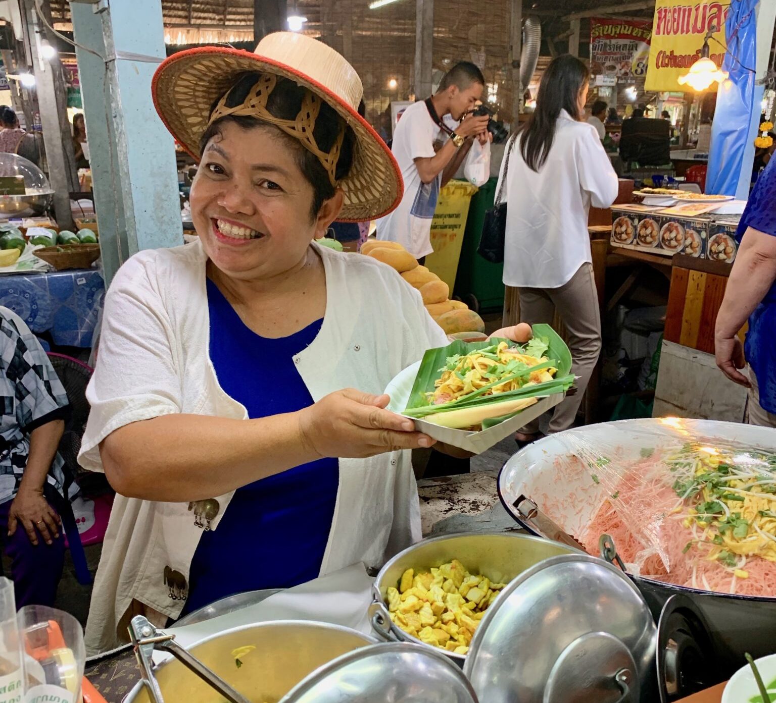 Venditrice sorridente offre cibo locale in mercato tailandese. IMG_0670. Sapori autentici, atmosfera vivace.