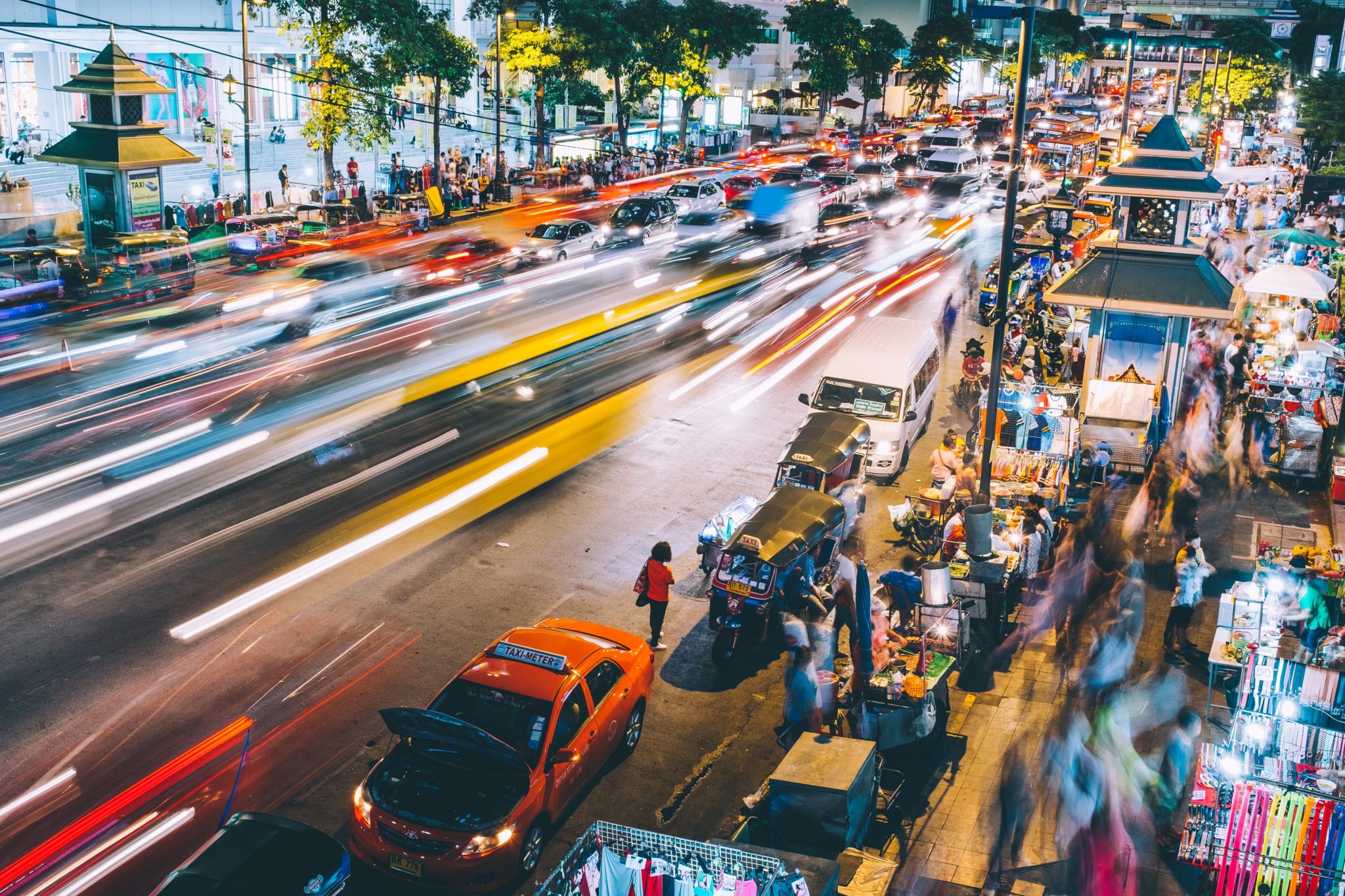 Traffico notturno a Bangkok. Auto, taxi e persone creano una scena urbana dinamica e illuminata, piena di vita.