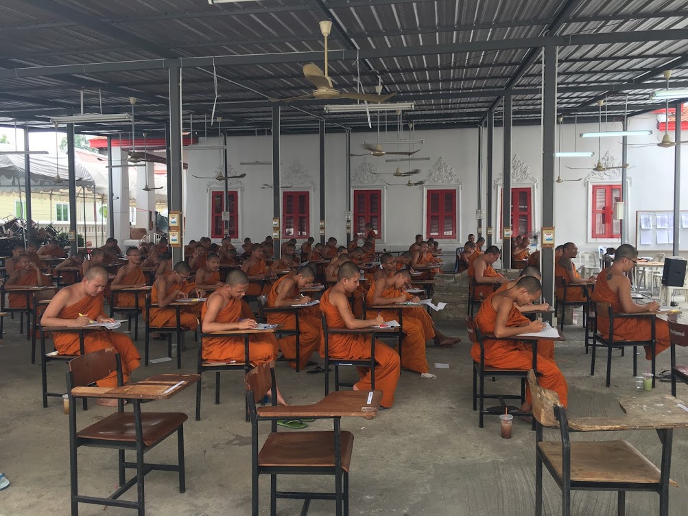 : Monaci buddisti in arancione scrivono ad un esame in un'aula. Concentrazione e studio.