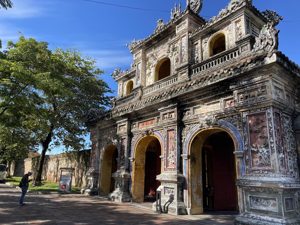 Viaggio Vietnam: Porta storica decorata, Hue. Architettura vietnamita antica e persona in primo piano.