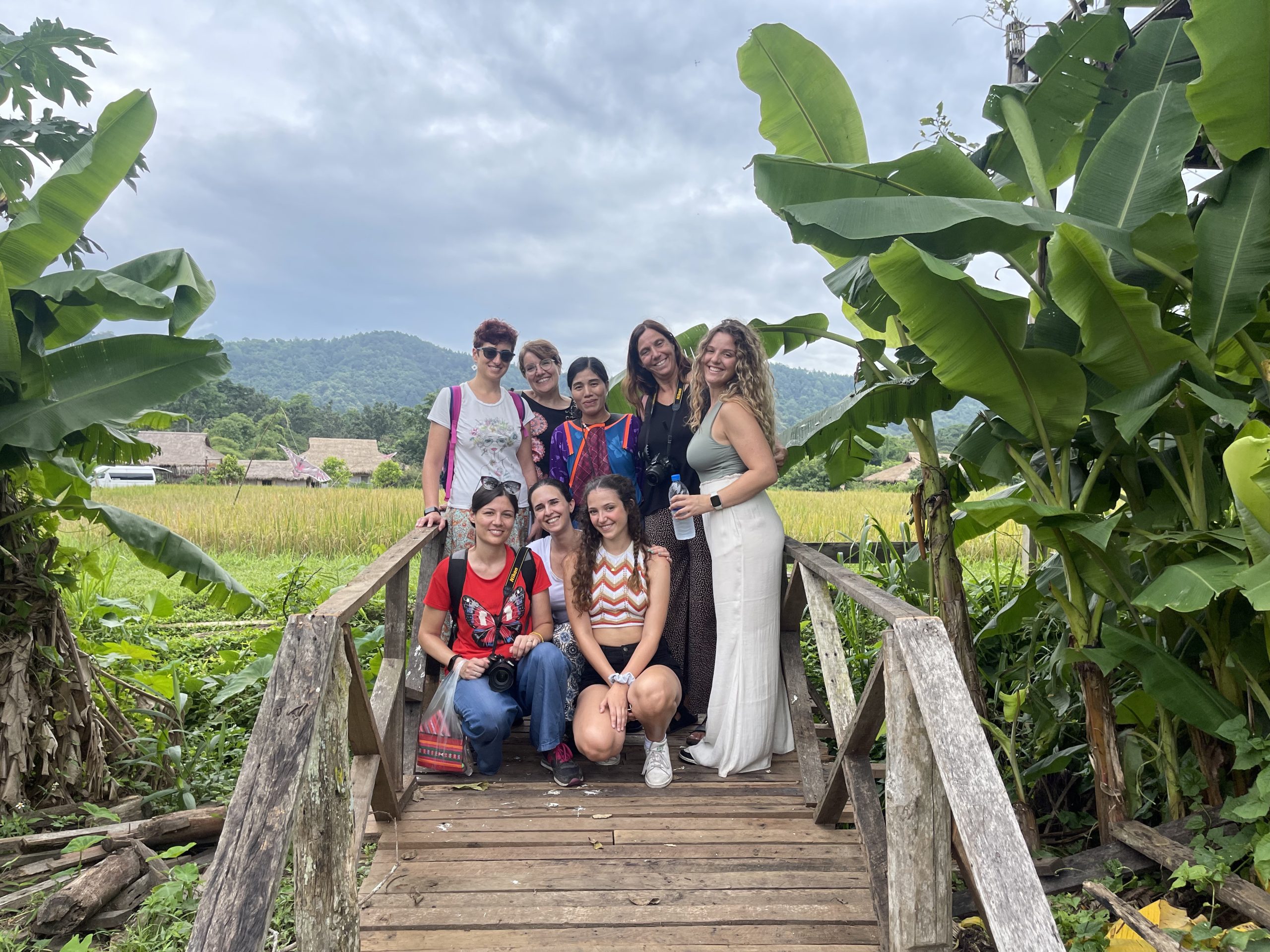 Chi sono: Gruppo di donne sorridenti su ponte di legno in campagna, vegetazione lussureggiante.